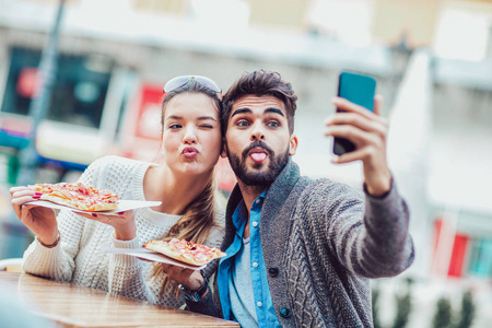 夫妇吃比萨饼户外和制作自拍照片上智能手机