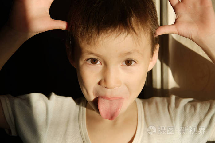 男孩开玩笑孩子气的恶作剧肖像与舌头在阳光下.