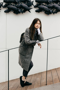 深色头发的城市女孩穿着灰色的衣服站在一个不寻常的建筑, 街道风格的台阶上