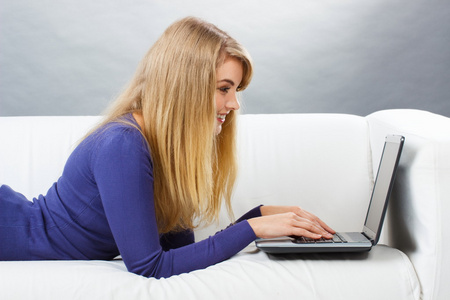 幸福的女人用笔记本电脑躺在沙发上现代科技