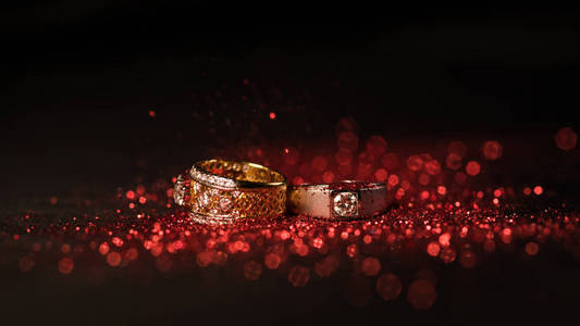 金色结婚戒指红色闪光和红色散景在黑色背景上