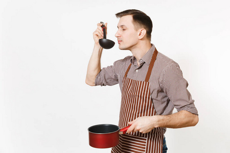 年轻人厨师或侍者在条纹褐色围裙, 衬衣举行和品尝红色空的 stewpan 黑钢包被隔绝在白色背景。男管家或 houseworke