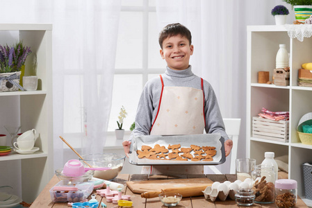 男孩展示了一盘烘烤饼干在家庭厨房内部, 自制的食物概念