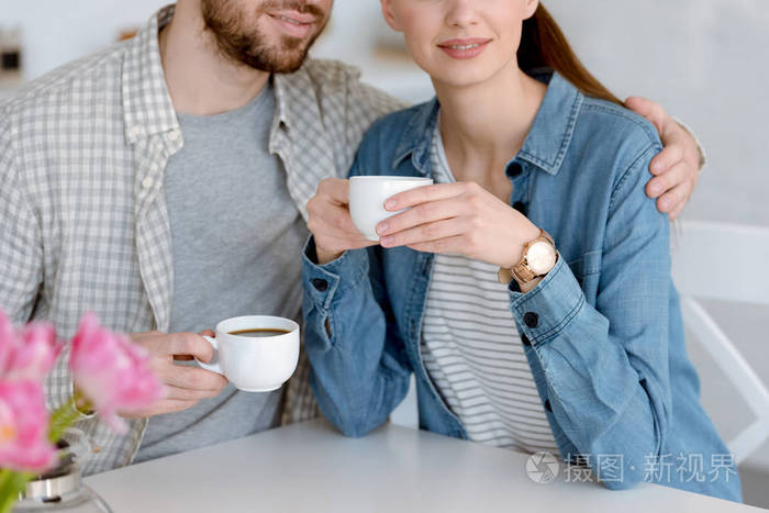 在厨房里坐着咖啡杯的情侣的裁剪视图