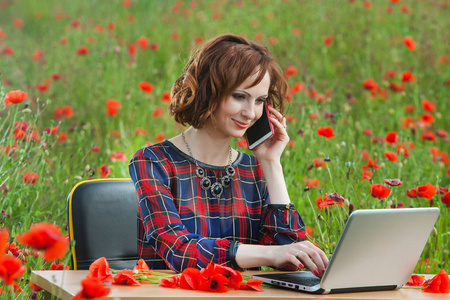 一个美丽的年轻女子坐在一张桌子，在字段中使用计算机的业务概念镜头。在阳光明媚的草地自然办公室的年轻商人。笔记本电脑以外的年轻女子