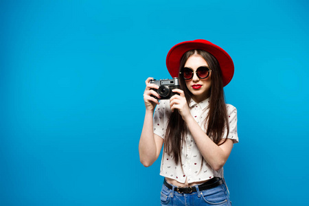 时尚年轻漂亮微笑女人抱着复古相机戴顶红色的帽子，在蓝色的背景