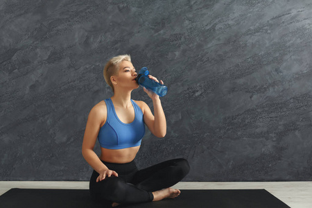 健身妇女在健身房喝水的灰色背景