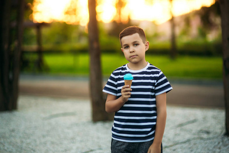 一个穿着条纹 t 恤的小男孩正在吃蓝色冰激淋。春天，阳光明媚的天气