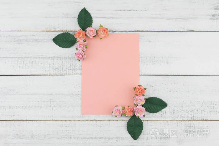 空白粉红色卡片装饰与粉红色玫瑰色纸花和绿叶在白色木头背景
