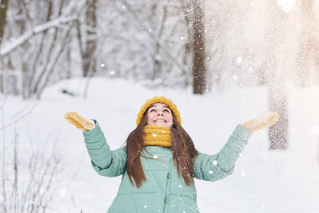 一个戴着针织帽子的漂亮女孩在冬天的森林里扔雪。