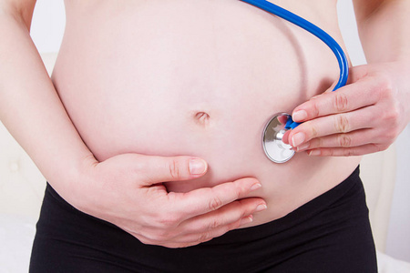 怀孕妇女与听诊器在腹部听日图片