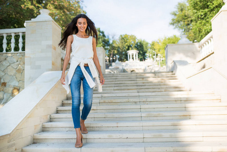 全身肖像的年轻微笑的黑发妇女走下台阶, 公园的楼梯照片