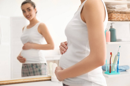 美丽的怀孕妇女在镜子附近在早晨