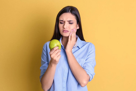 彩色背景的敏感牙齿和苹果的年轻女子照片