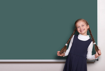 辫子的女孩美丽的学校附近空白的黑板背景，穿着经典的黑色西装，教育概念笑了