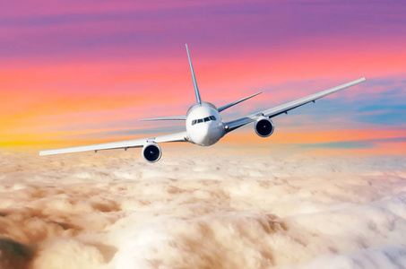 客机上的飞机在云层上空飞行, 地平线上有明亮的日落颜色.