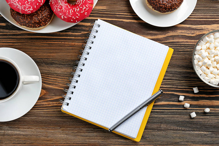 美味甜甜圈与杯咖啡和笔记本