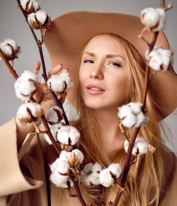 妇女在帽子在柔和的颜色轻的褐色外套举行自然棉花花