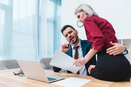 在办公室与文件一起工作的商人拥抱诱人的女性同事照片