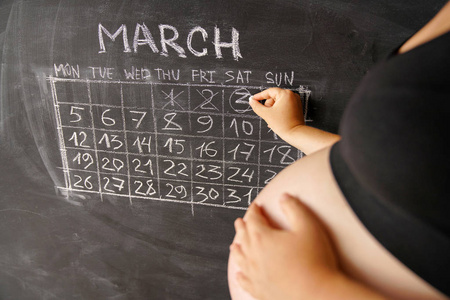 怀孕妇女的日历在月3月计数天以日历为孩子的诞生在黑板上。怀孕的概念
