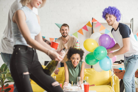 快乐的年轻人在生日聚会上看着女人开香槟照片