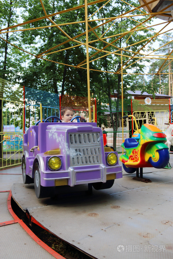 英俊的小男孩骑在车在游乐园里的旋转木马