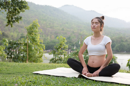 亚洲孕妇练瑜伽在公共 pa 的绿色草地上