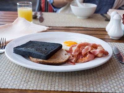 早餐与营养有面包木炭, 土司, 培根和鸡蛋在一个白色的盘子. 背景橙汁盐和胡椒粉