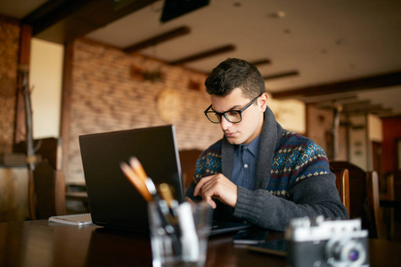 沉思英俊的男子博客更新他的个人资料在社交网络与照片分享与追随者多媒体文件坐在咖啡馆与摄像头和笔记本电脑与 wifi。眼镜书