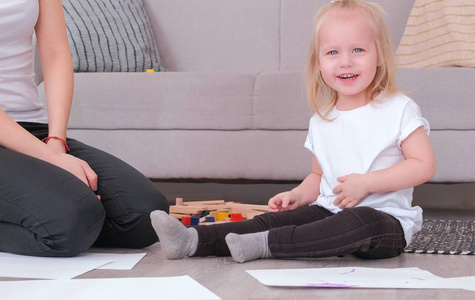 小可爱的金发女孩玩木块与她的妈妈坐在沙发附近