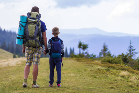 父亲和儿子带着背包徒步漫步在风景秀丽的夏绿山上。爸爸和孩子站在欣赏山水山景。积极的生活方式, 家庭关系, 周末活动的概念
