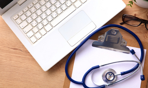 附近一台笔记本电脑上木桌前，在白色的医用听诊器