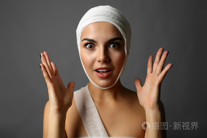 情感的年轻女子在她头上在灰色的背景上的纱布绷带