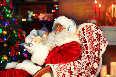 圣诞老人坐着耳机坐在舒适的摇椅上在家里