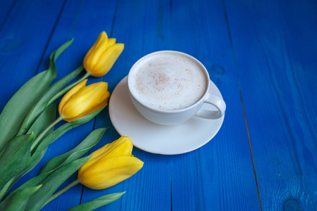 咖啡杯与黄色的郁金香花和蓝色仿古桌上注意到早上好