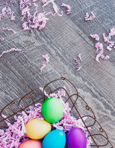 明亮的彩色复活节彩蛋坐在一个铁丝篮, 顶部的国家风格的木地板。这张彩色照片为您的节日设计提供了一个很好的背景和边框。