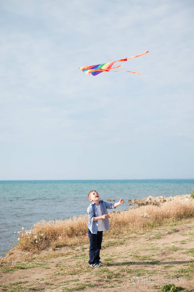 夏天可爱的小男孩抱着五颜六色的风筝在蓝天下翱翔在海边