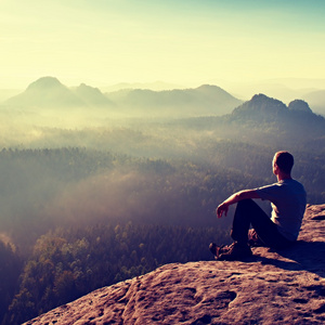 高短发徒步旅行者在光衬衫坐在一块岩石和享受雾山风光