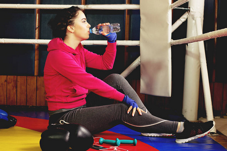 美丽的渴拳击女孩环中饮用的水。在健身房训练。运动女性做拳击运动
