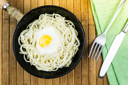 煎蛋和意大利面在一个黑色煎锅, 叉子和刀子。餐桌上的咖啡馆里的午餐