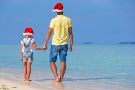 小女孩和快乐的父亲在圣诞老人的帽子在海滩圣诞假期