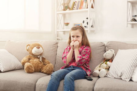 在家坐沙发的时候, 害怕的不经意的小女孩看电视照片