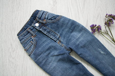 蓝色牛仔裤和花。木质背景。时尚理念