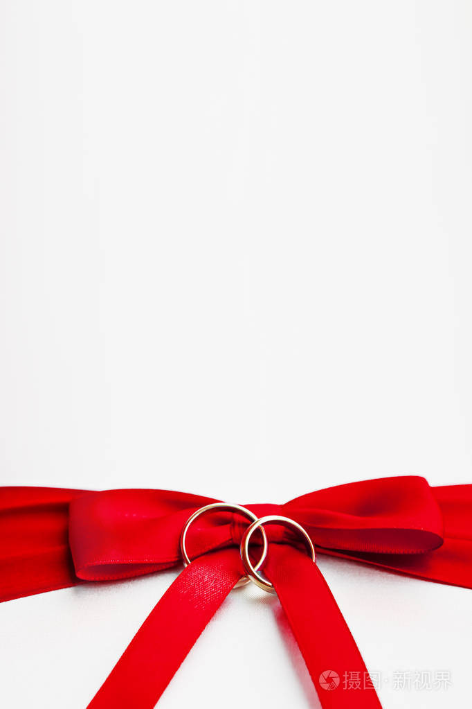 金色的结婚戒指上红弓上的白色丝绸背景.婚礼细节.爱情与婚姻的象征.