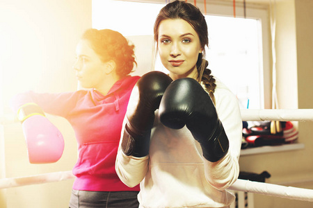 美丽的拳击女孩与黑人拳击手套合影的画像。在健身房训练。运动女性做拳击运动