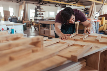 熟练的年轻木匠与胡子手打磨木制家具设计的部分, 而在他的大型木工店工作