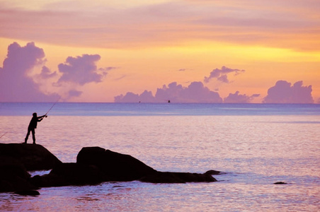 一个男人在日落时在海边的岩石上钓鱼。