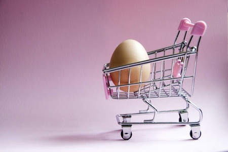 购物车。超市手推车上满是粉红色背景的大鸡蛋。消费主义概念照片