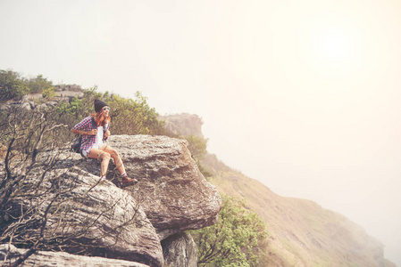 年轻的徒步旅行者背包坐在悬崖边上, 看着自然山谷和山脉。