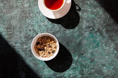 有烤麦片的盘子, 有浆果的燕麦片和一杯在绿色混凝土背景上的茶。